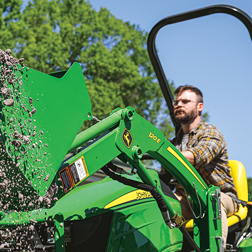 Man operating the loader on a John Deere compact tractor